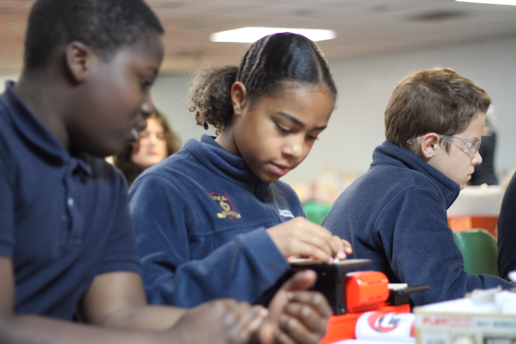 NOCA students in navy uniforms working carefully on a hands-on project at their table.