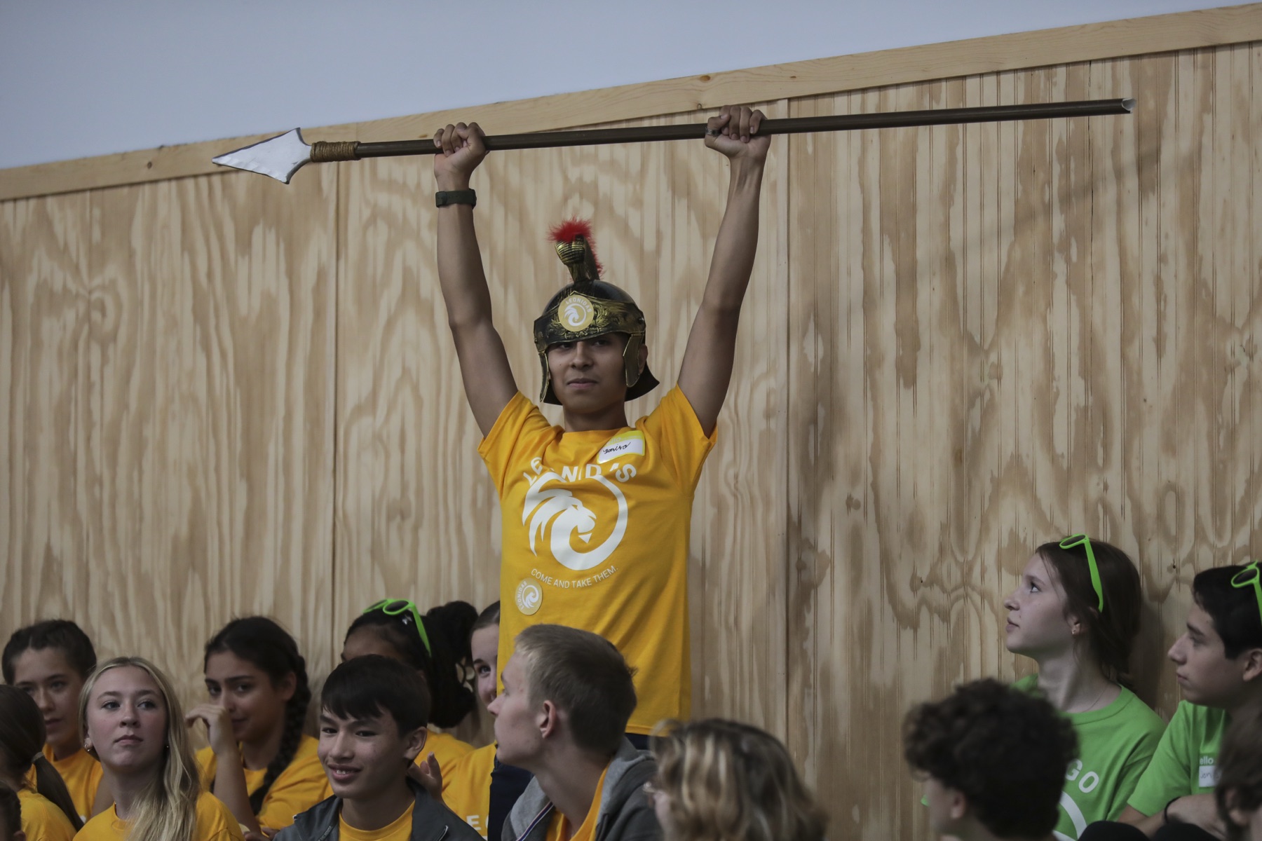 A NOCA student holds a prop spear overhead in a Spartan helmet during a house-competition event.